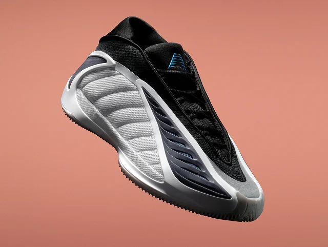 An Alphadawg black and white adidas Anthony Edwards 2 basketball sneaker shown angled against a orange background. It has a sculpted sole and wave-like side design.