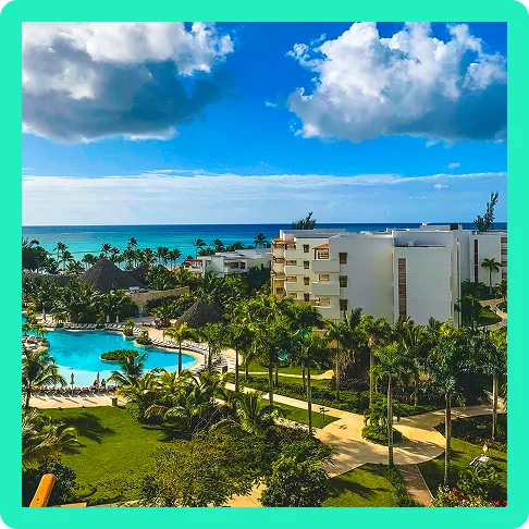 Image Description: A zoomed-out view of a resort with tropical greenery and a large pool with the ocean just beyond.