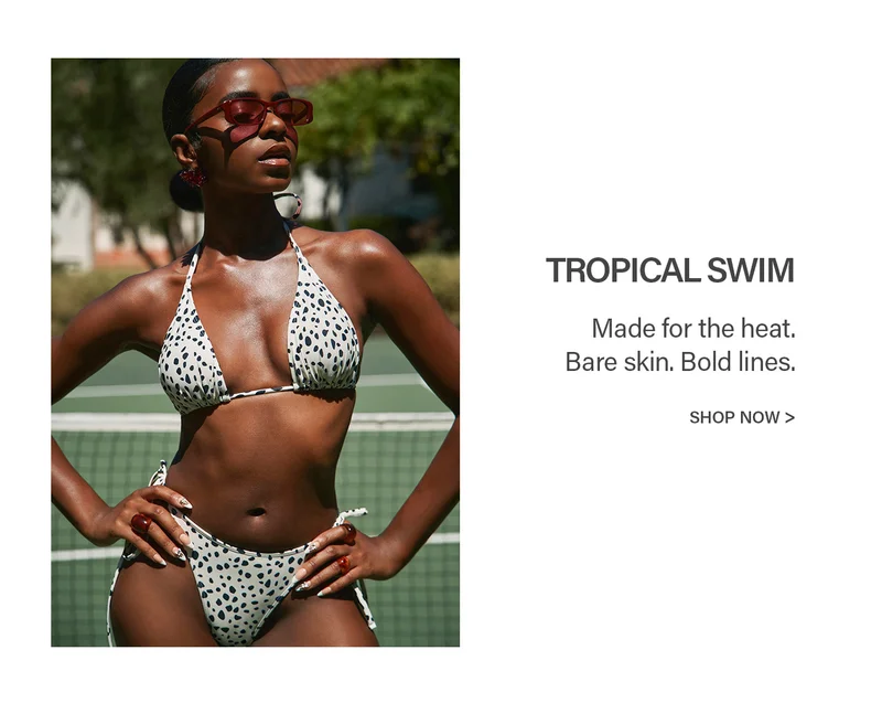 Confident model in a spotted white bikini, red sunglasses, posing on a tennis court. Shop our vibrant tropical swim collection.
