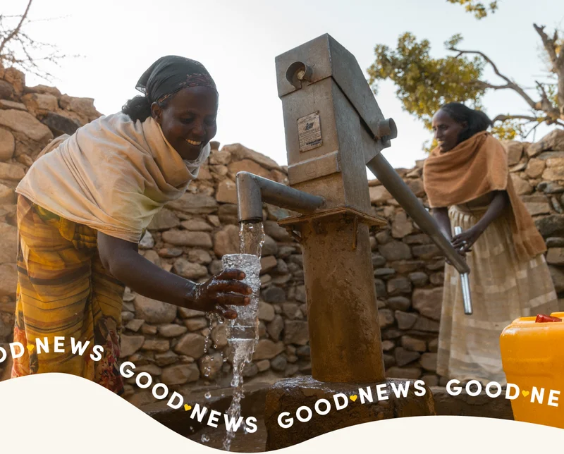 Two young women pump water from a hand pump.