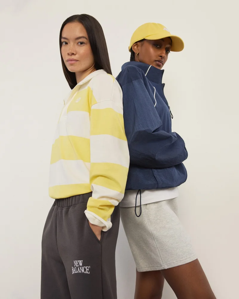 A stack of New Balance shoe boxes next to a shopping bag against a pale apricot backdrop