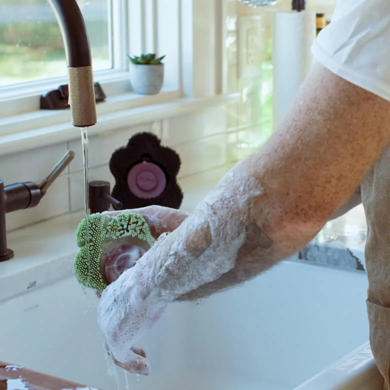 Person washing their arms with a Smoosh body scrubber at the sink