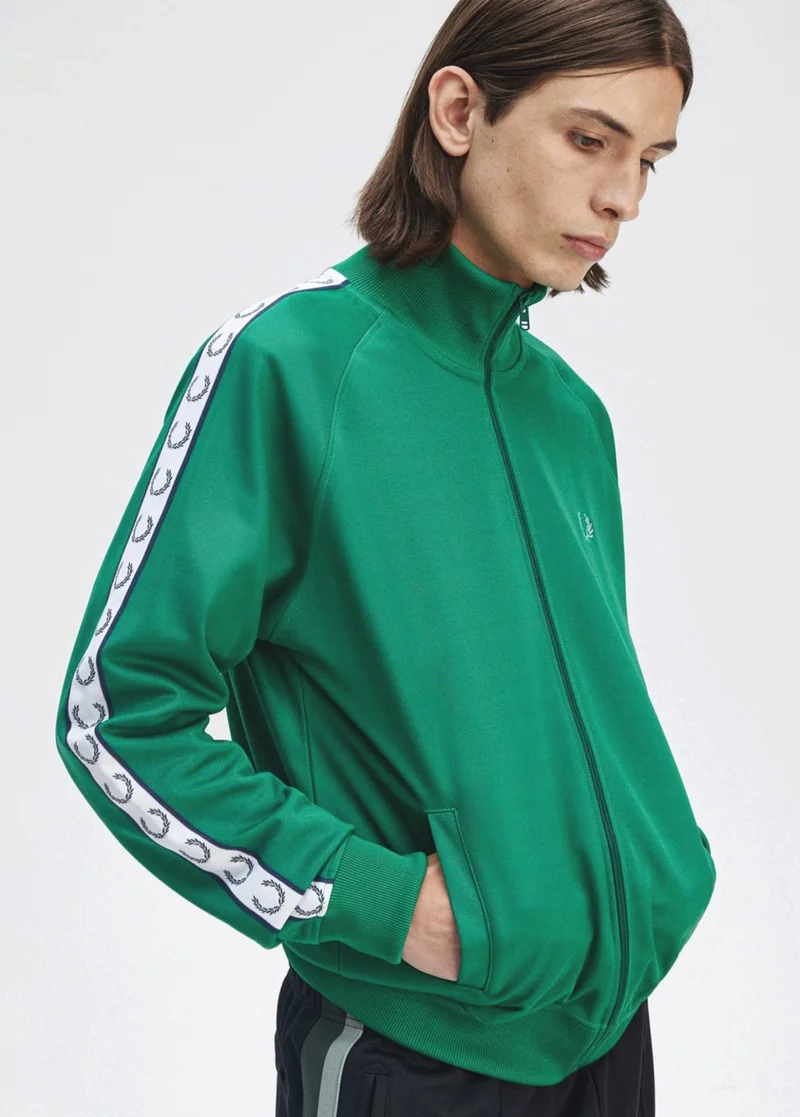 A white model wearing a Fred Perry Taped Track Jacket in Label Green