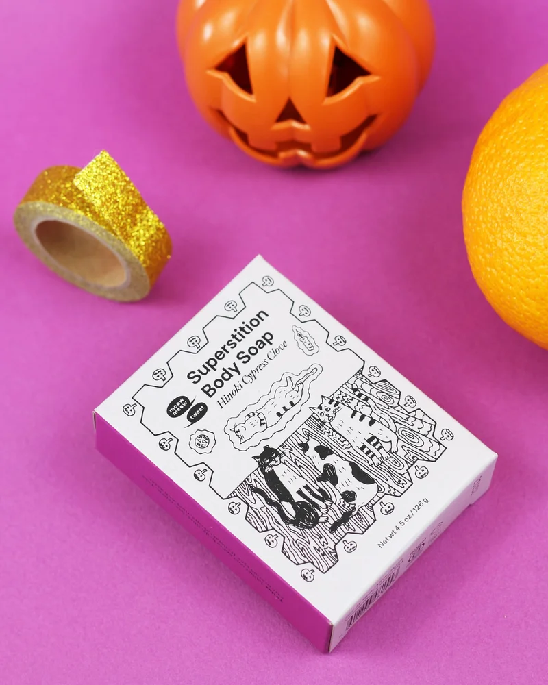 A grey box of soap is laying on a magenta background with a plastic jackolantern and gold tape and orange surrounding it.