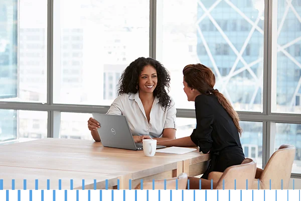 two womens talking in a room working on laptop