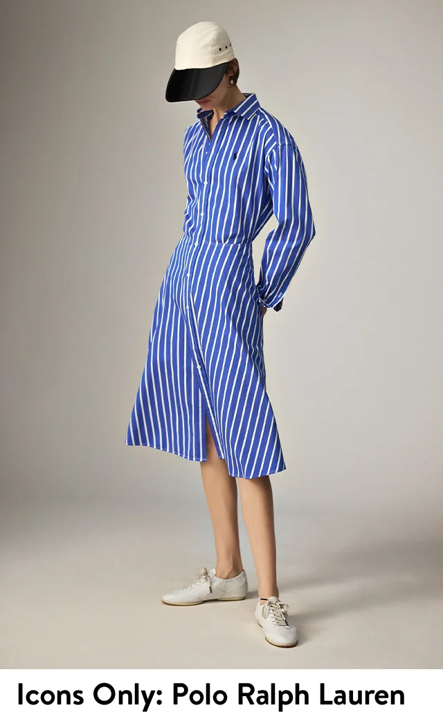 A woman wearing a striped shirtdress, baseball cap and sneakers.