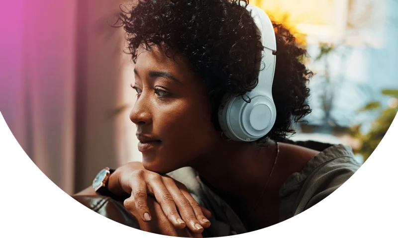 Shot of a young woman looking thoughtful while wearing headphones at home