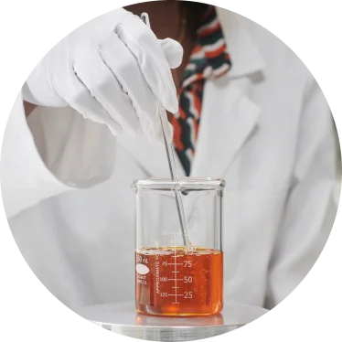 Person in lab coat drawing solution from a beaker.