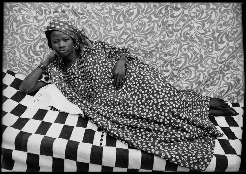 A portrait of a woman in a floral dress lounging on patterned textiles