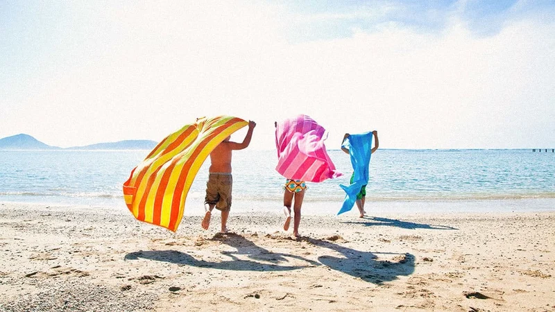 Image description: Family running with colorful towels on beach in Oahu
