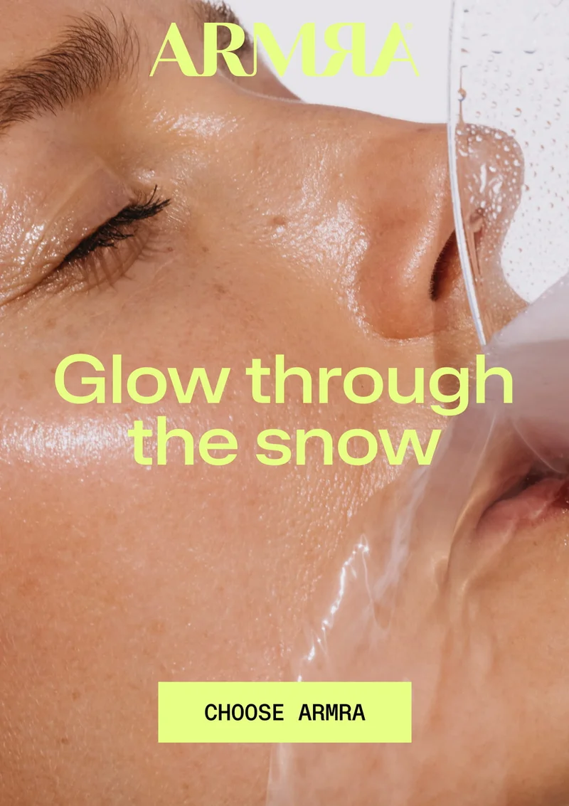 Close-up of glowing skin with water splashing across the face and headline reading “Glow through the snow” with a Choose ARMRA button.