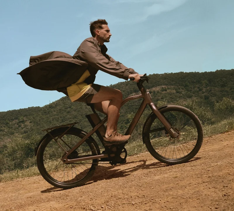 A photograph. A rider on a Cowboy Cross, his coat bollowing out behind him as he effortlessly climbs a hill.