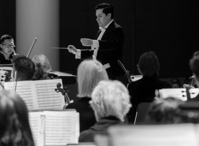 A black-and-white photo of a conductor leading an orchestra