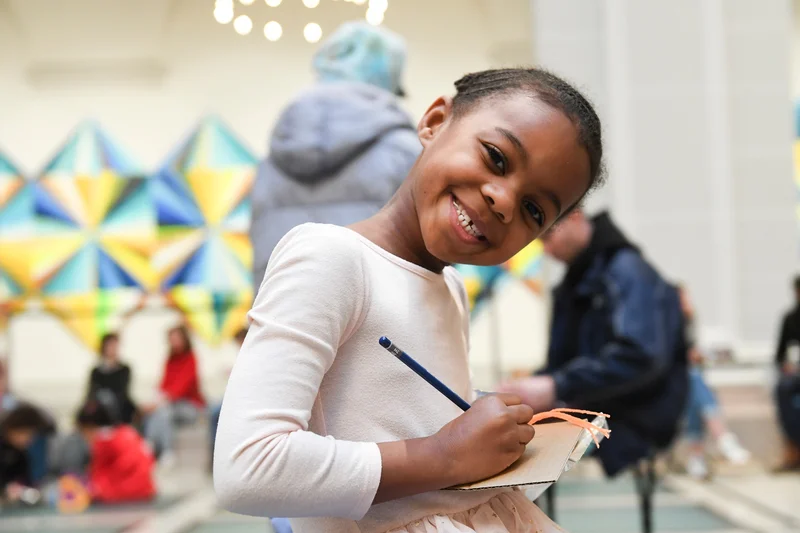 A girl holding a pencil and paper and smiling