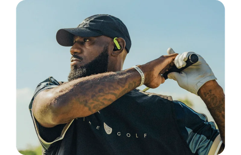 LeBron James swinging a golf club wearing the special-edition Nike Powerbeats Pro 2 earbuds.