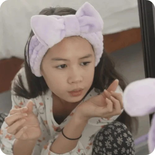 teen doing her skincare routine in the mirror wearing a purple terry headband teen doing her skincare routine in the mirror wearing a purple terry headband
