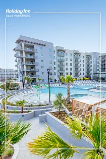 White villas with palm trees beside a bright blue pool.