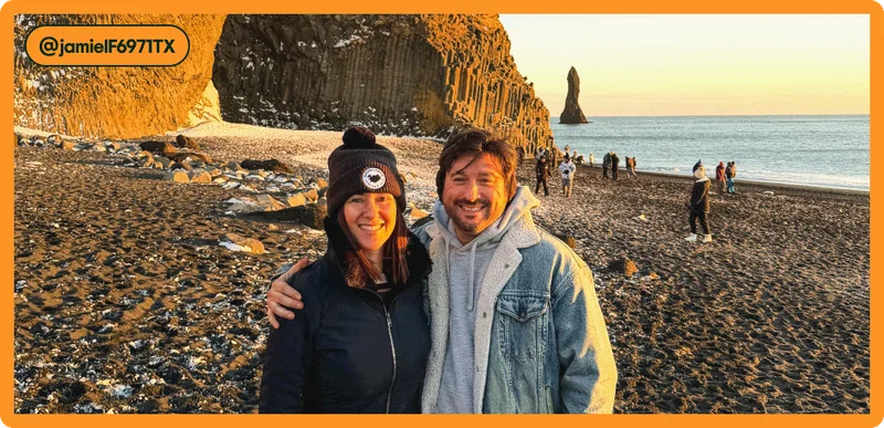 Image Description: Man and a woman smile and pose for a photo on a black sand beach with large rock formations and the ocean in the background.Tag attribution in the corner for user @jamielF6971TX.