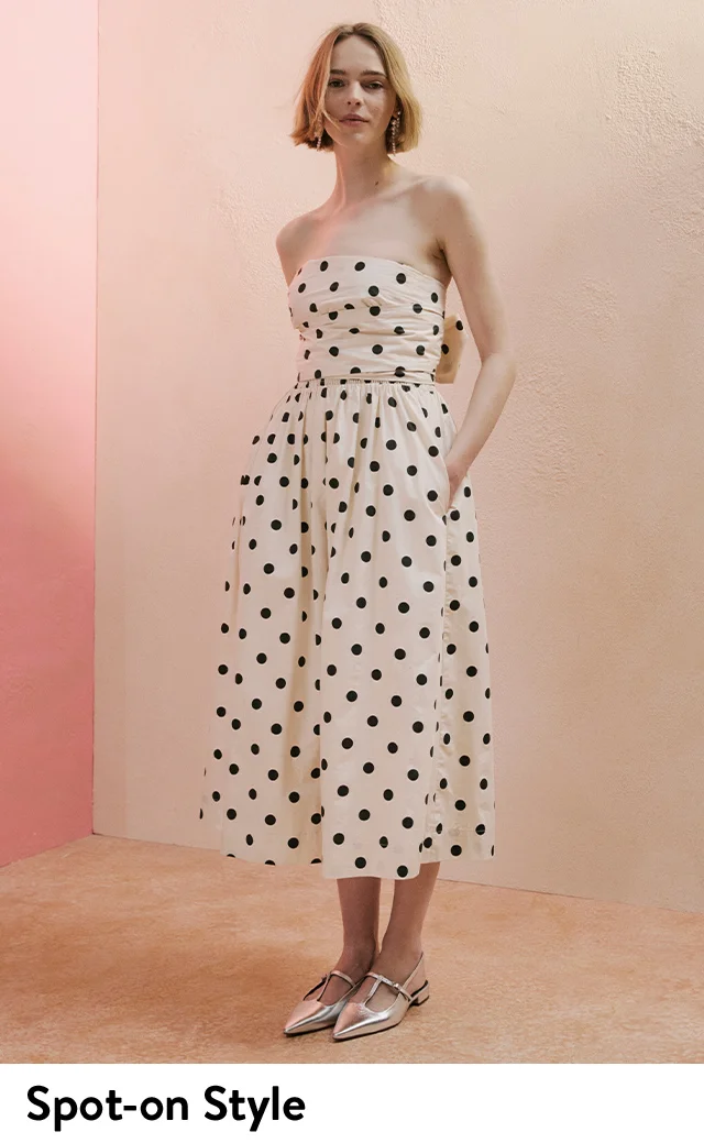 A woman wearing a strapless polka dot dress with silver flats.
