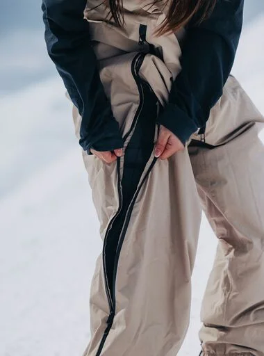 The Burton Futuretrust 2L Bib Pants in beige on a Burton Rider at a mountain on a sunny day