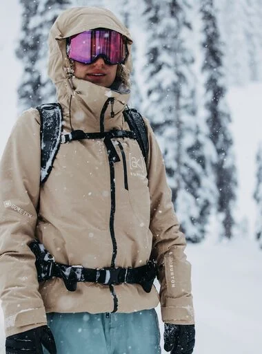 The Women's Burton [ak] Embark GORE‑TEX 2L Jacket in beige on a model in the snowy mountains