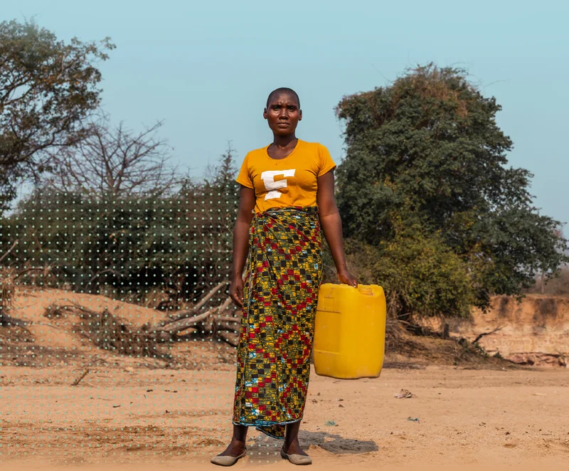 Loveness stands looking at the camera while holding a yellow jerry can.