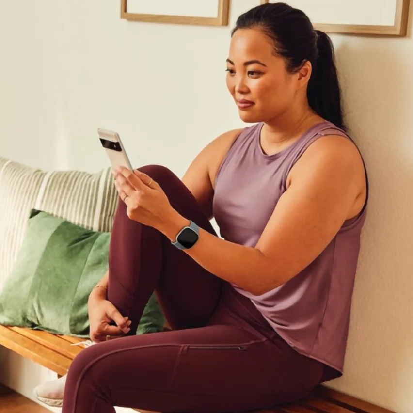 Woman in athletic wear using a smartphone while sitting on a wooden bench.