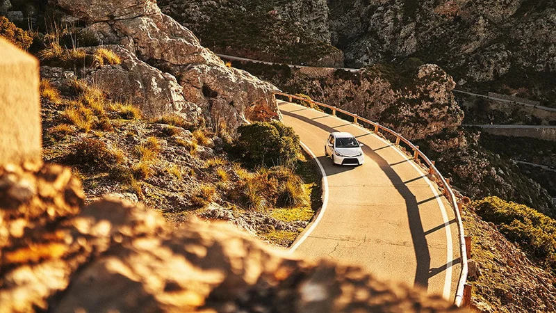Image description: Vehicle driving through mountains in summer