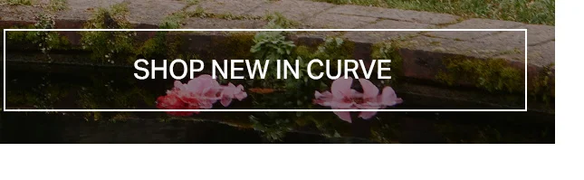 Two soft pink flowers float on dark reflective water next to a mossy stone wall. Banner for 'Shop New In Curve' plus-size fashion.