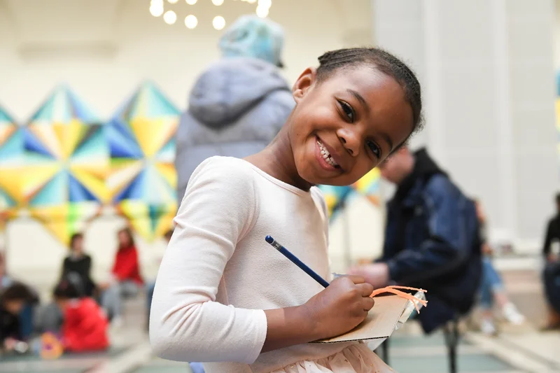 A photograph of a child smiling and drawing