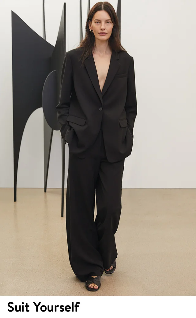 A woman wearing an oversized black blazer, relaxed wide-leg trousers and black sandals.