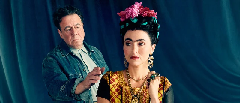 A woman with an elaborate headpiece and a man reaching for her shoulder