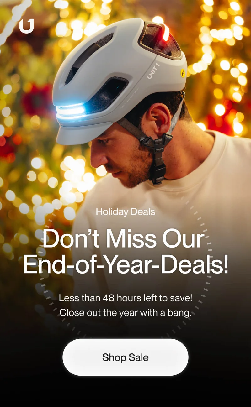 Man wearing a Unit 1 smart helmet with illuminated front and rear lights, set against a festive backdrop of golden holiday lights. Text reads 'Don’t Miss Our End of Year Deals!' emphasizing urgency with less than 48 hours to save.