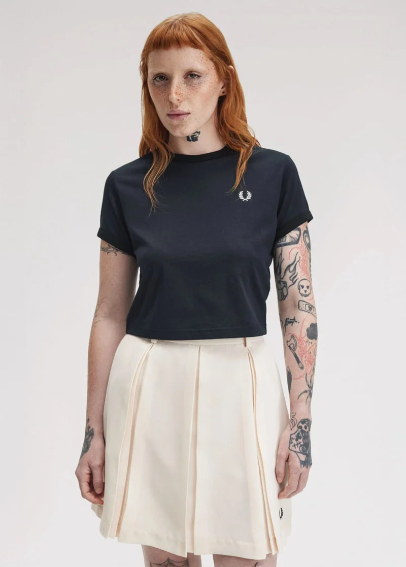 Long haired ginger woman wears navy T-shirt and ecru pleated short skirt