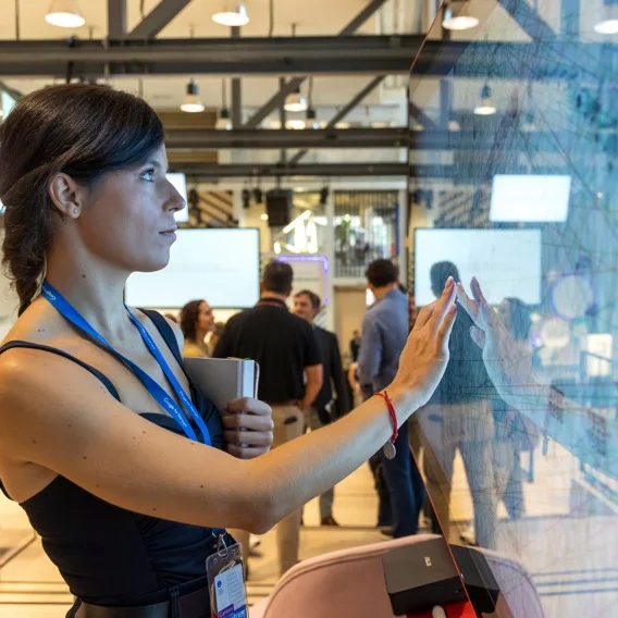 Photo of a woman looking at a large, semi-reflective touch screen lit up by lights. She holds her palm to the screen.