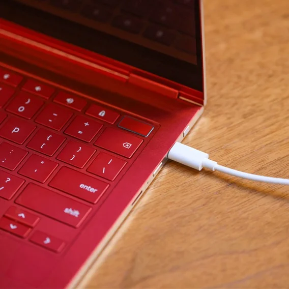 An open red Chromebook with a white cord stretching to plug into it.