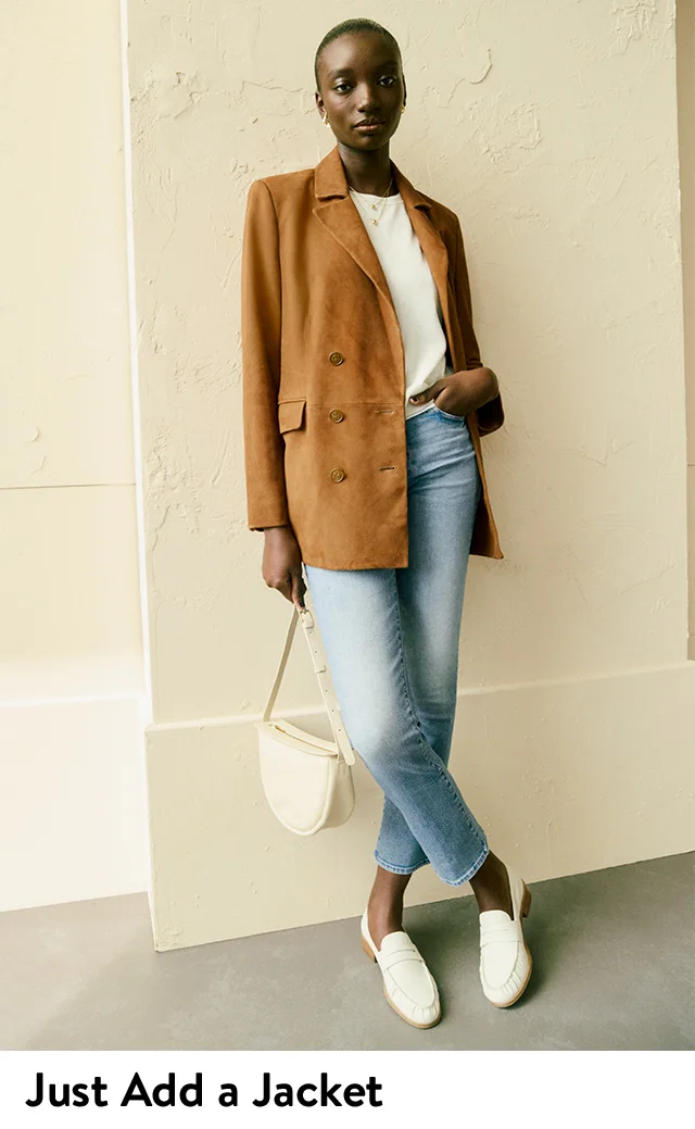 A woman wearing a light-brown jacket with a white tee and blue jeans.