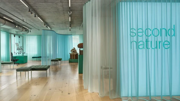 An open space with hardwood floors decorated with a variety of seating and sheer curtains that read second nature