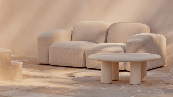 An outdoor Muse Sofa in cream upholstery and small table in the same color on a patio.