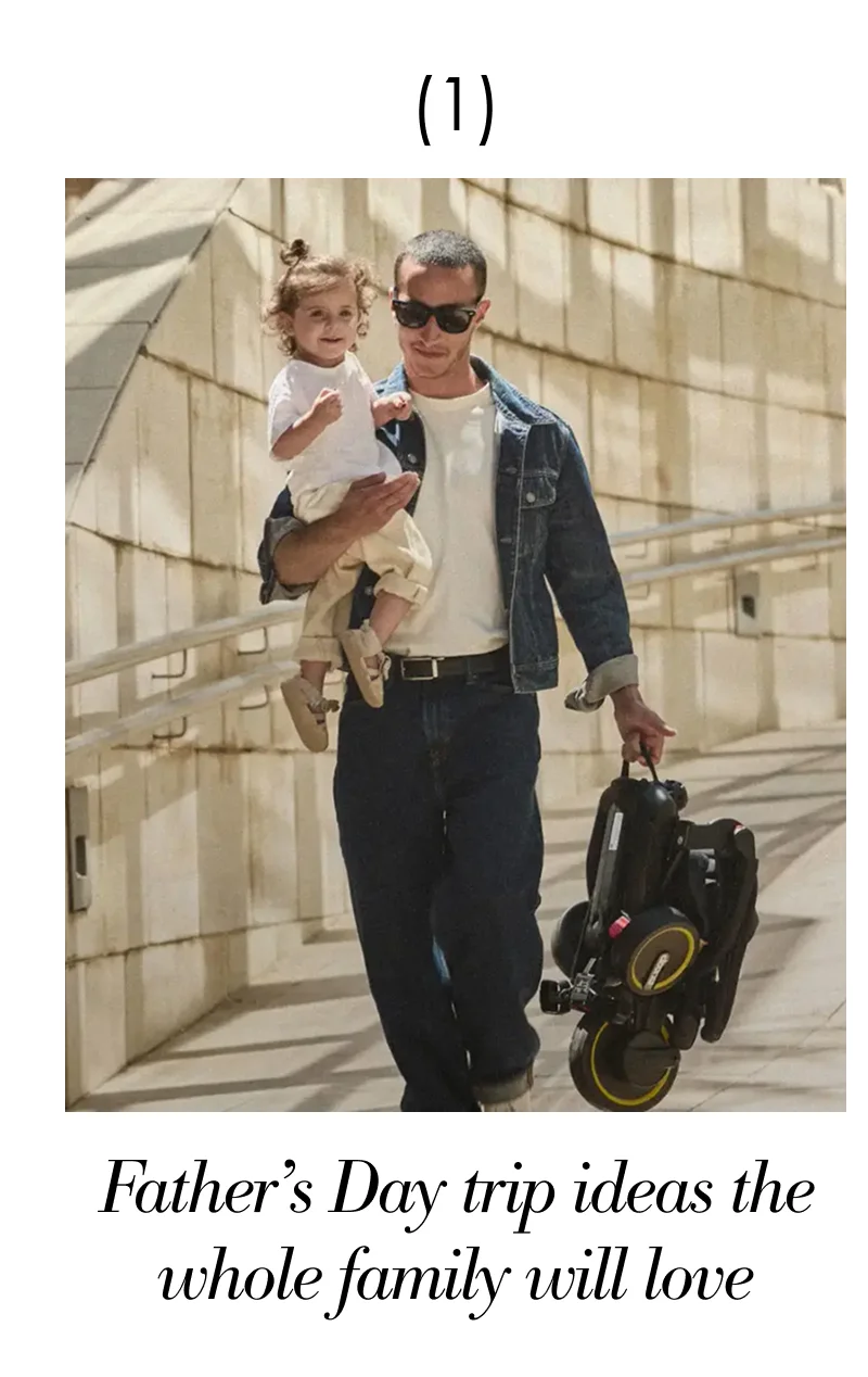 Man holding a toddler and carrying a Liki Trike during an outdoor family outing.