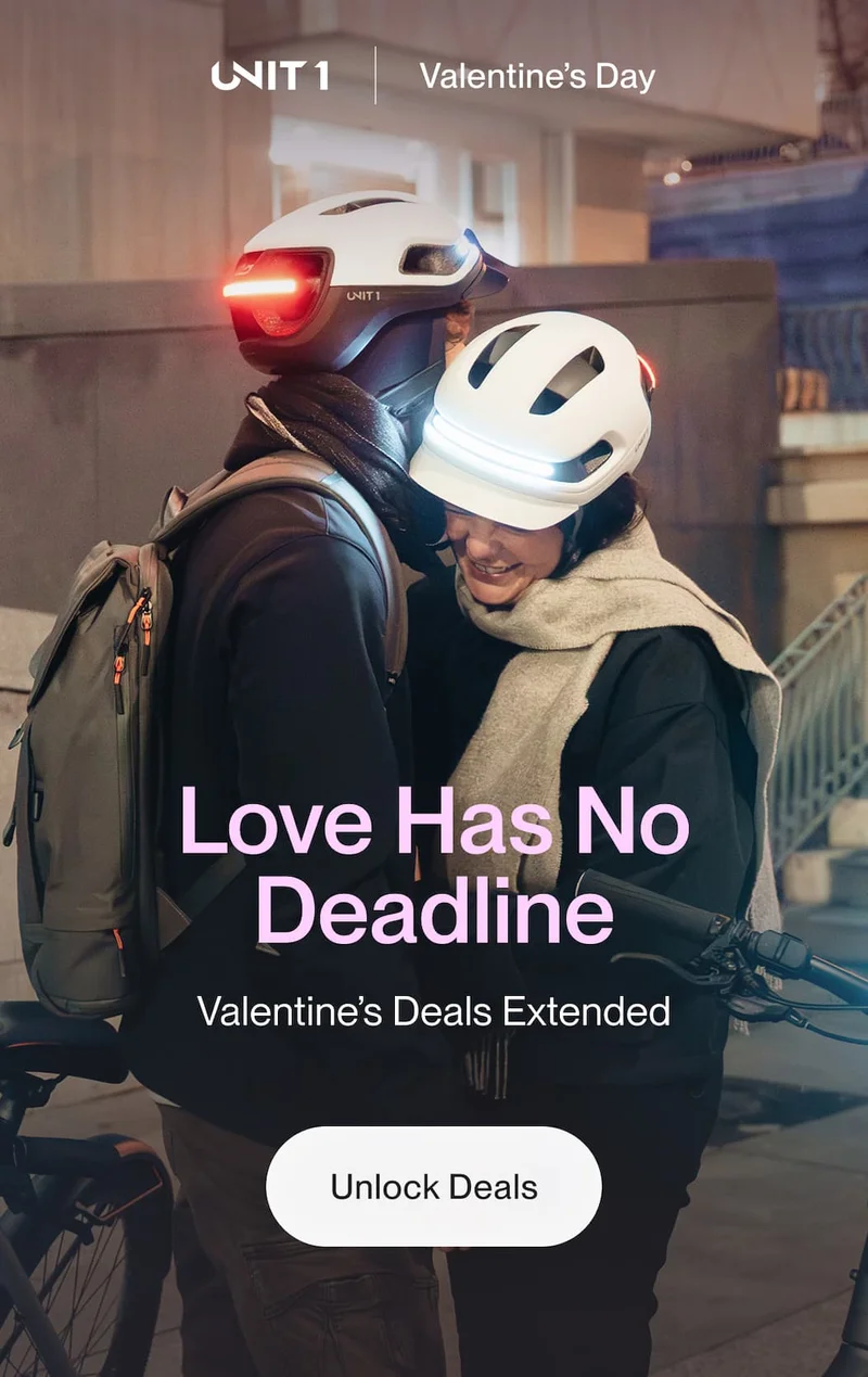 Couple wearing UNIT 1 smart helmets with front and rear lights illuminated, embracing beside their bikes in an urban setting at night.