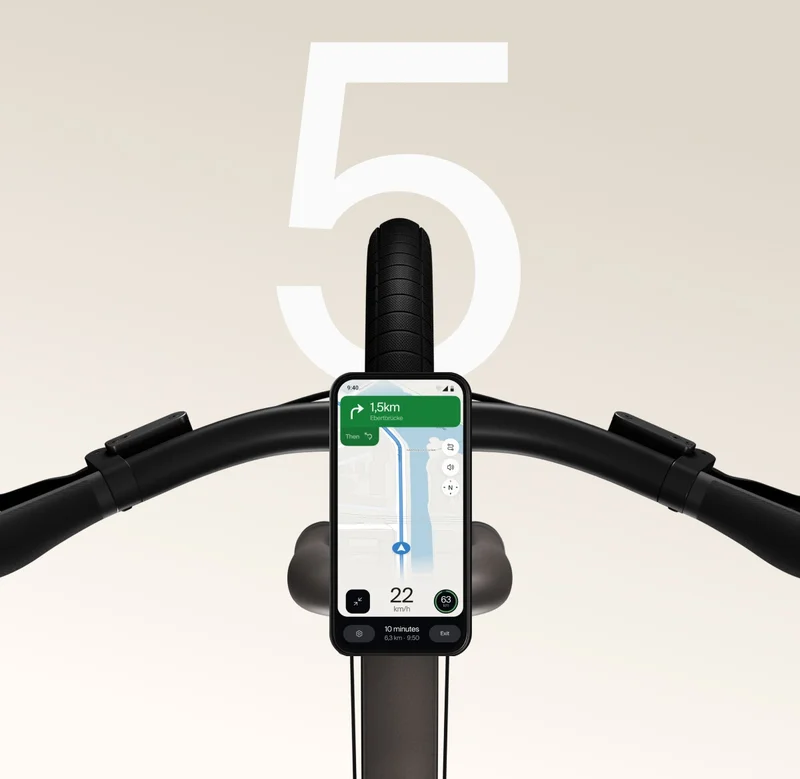 A Cowboy bike with a smartphone mounted on the handlebars, displaying navigation directions and speed on the app interface. A large white number “5” is visible in the background.