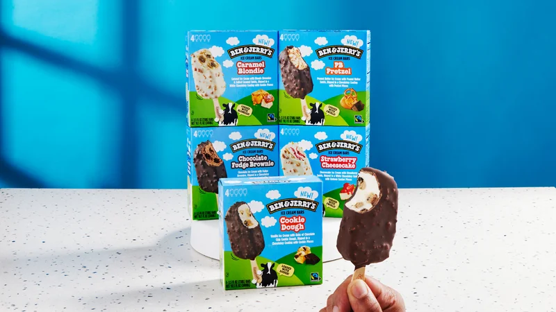 Five packages of new Ben & Jerry's Ice Cream Bars. Hand holding a bar with a bite taken out.