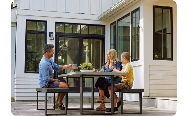 A family having coffee outside with an Arlo security camera mounted on the exterior of their home.