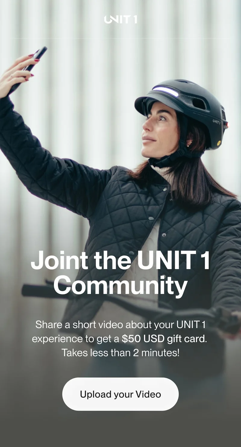 Woman riding a bike while wearing a UNIT 1 smart helmet with front light on, holding her phone and recording a video.