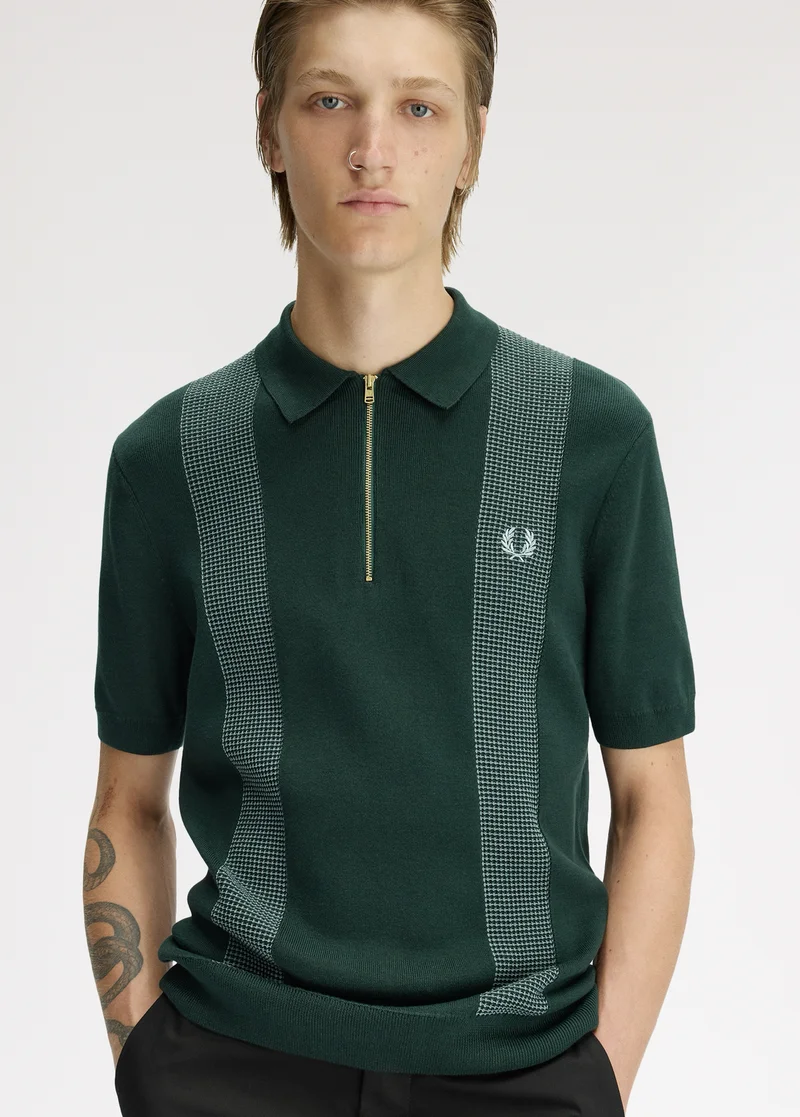 New Releases" Blonde male model looks into the camera with his hands in his pockets and wears a dark green zip knitted polo shirt with white and dark green waffle panelling on either side of his chest