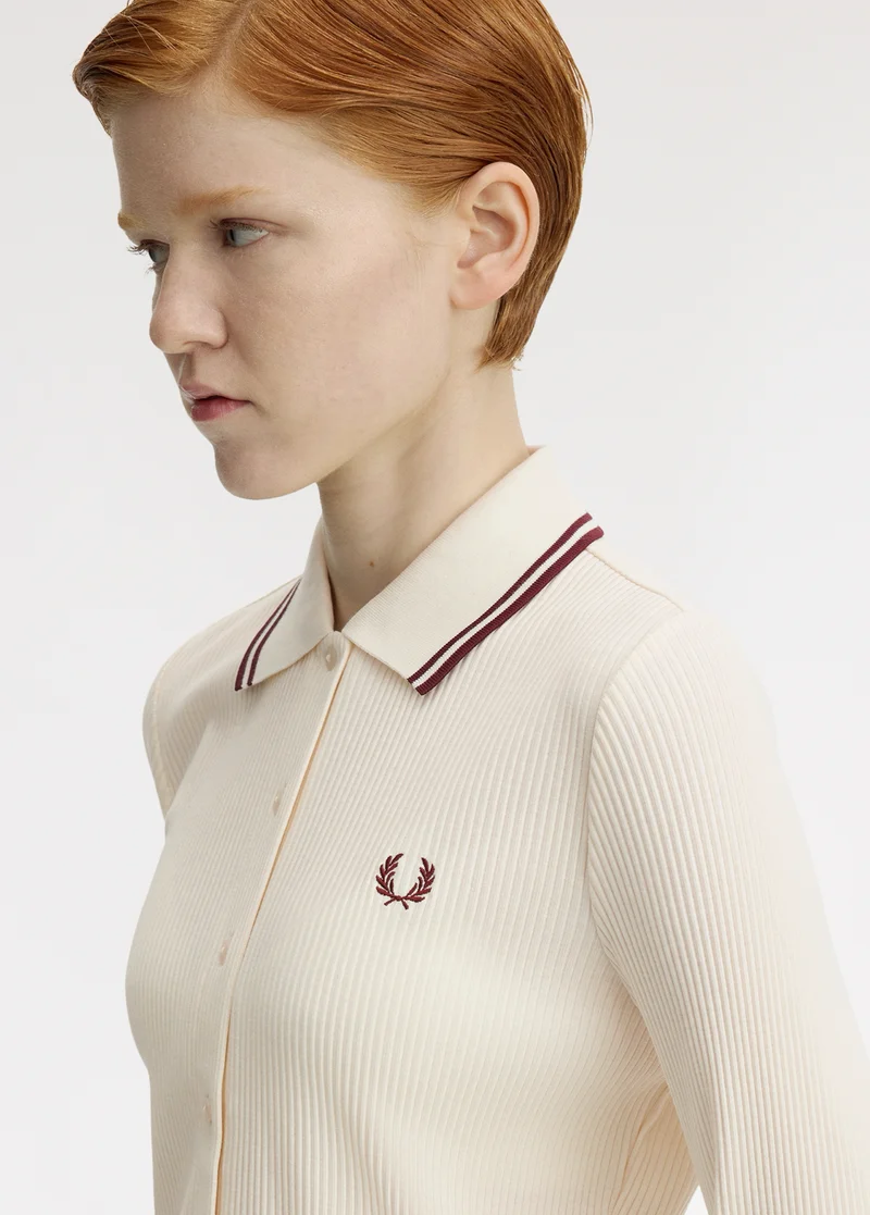 New Releases: pale female model with short ginger hair looks to the side and wears a ribbed ecru long sleeve shirt with a polo collar with oxblood twin-tipping
