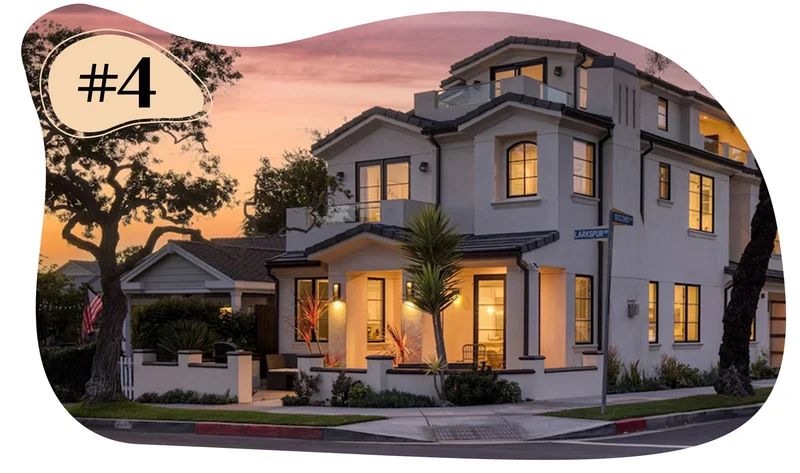 Two-story corner house at sunset with balconies, large windows, and exterior lights on.