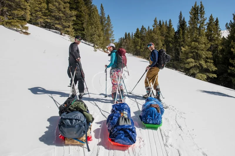 Three backcountry skiers pulling sleds.