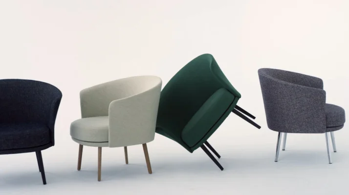 A whitesweep photo of Dorso chairs lined up in a row with a navy Dorso chair on the right facing forward, a cream Dorso chair on a left diagonal, a dark green Dorso chair tilted on two legs and leaning against the cream Dorso chair, and a dark gray Dorso chair facing right.